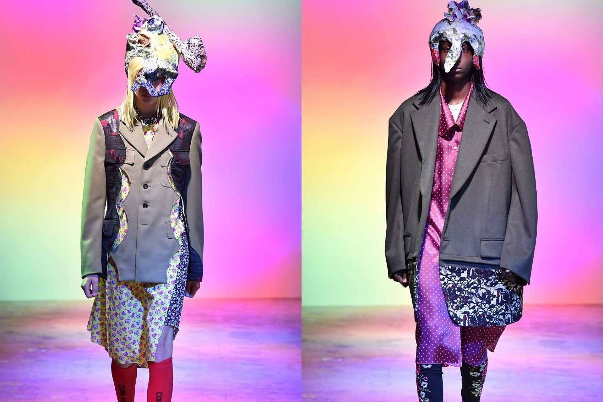Two models wearing deconstructed suiting and sculptural head masks/hats in front of rainbow gradient backgrounds