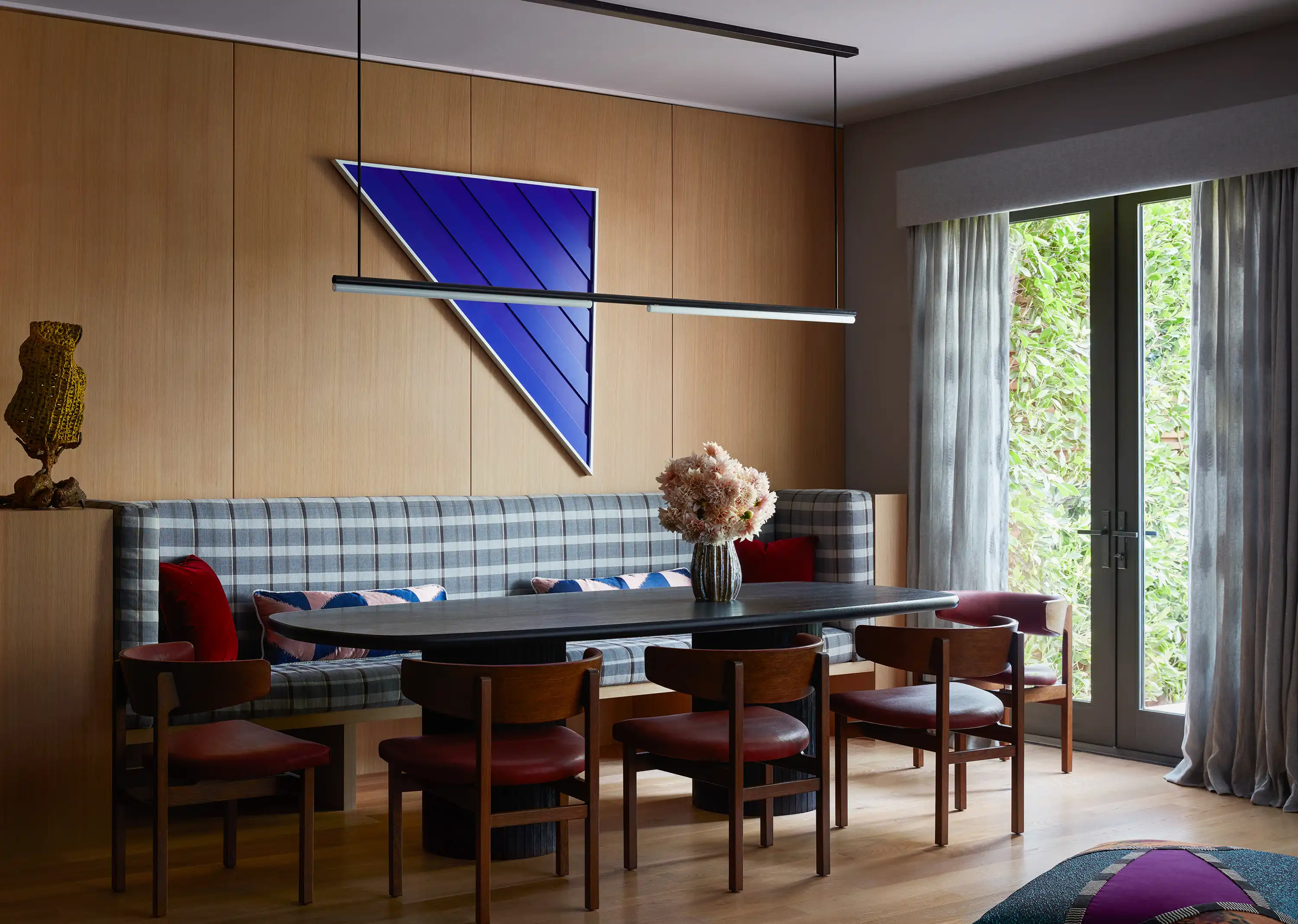 Vintage Børge Mogensen dining chairs in Howe leather and a Rudolph Schindler-inspired banquette in a Lauren Hwang fabric—plush with Chroma pillows in Claremont red velvet and a Pierre Frey fabric—embrace a custom black-stained Chroma dining table with Shou Sugi Ban base.