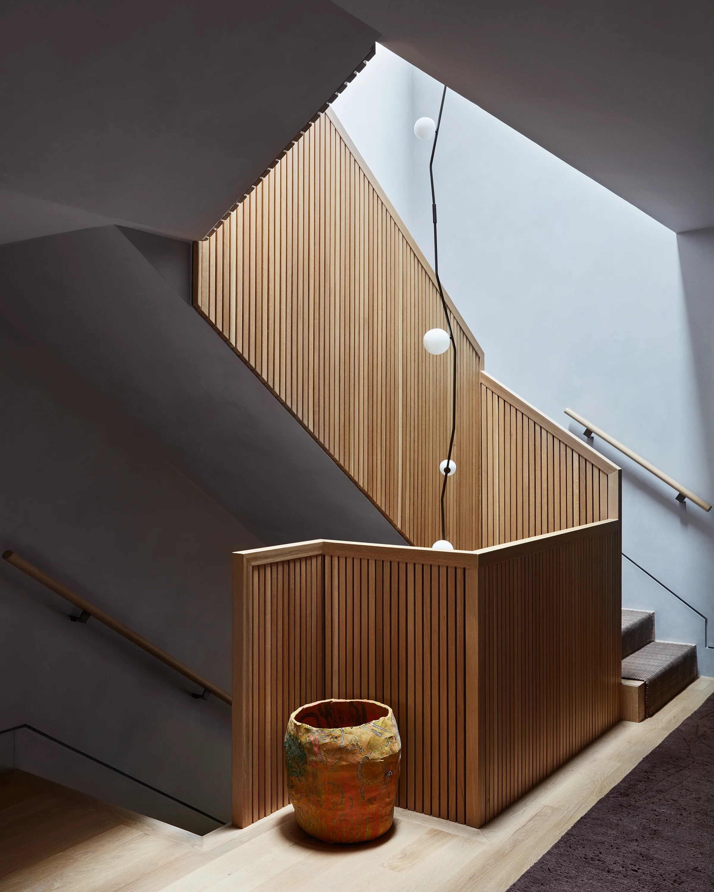 A Cherry Bomb Chandelier by Lindsey Adelman Studio twines within the elegant craft of the custom staircase accentuated by a Roger Herman ceramic.