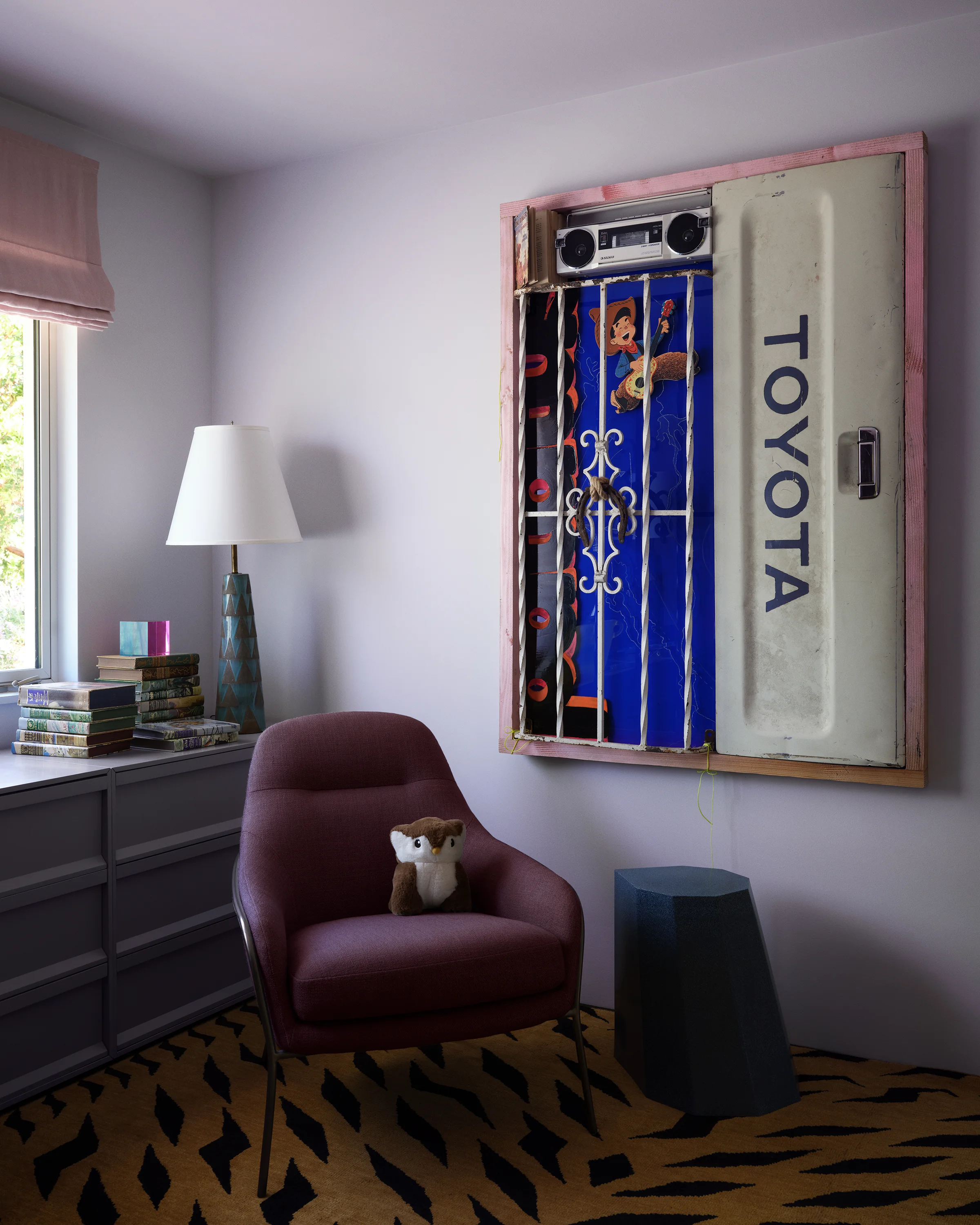 Contemporary artworks create a playful assemblage above burgundy velvet chair with graphic tiger print rug in eclectic Sonoma kids' bedroom designed by Chroma.