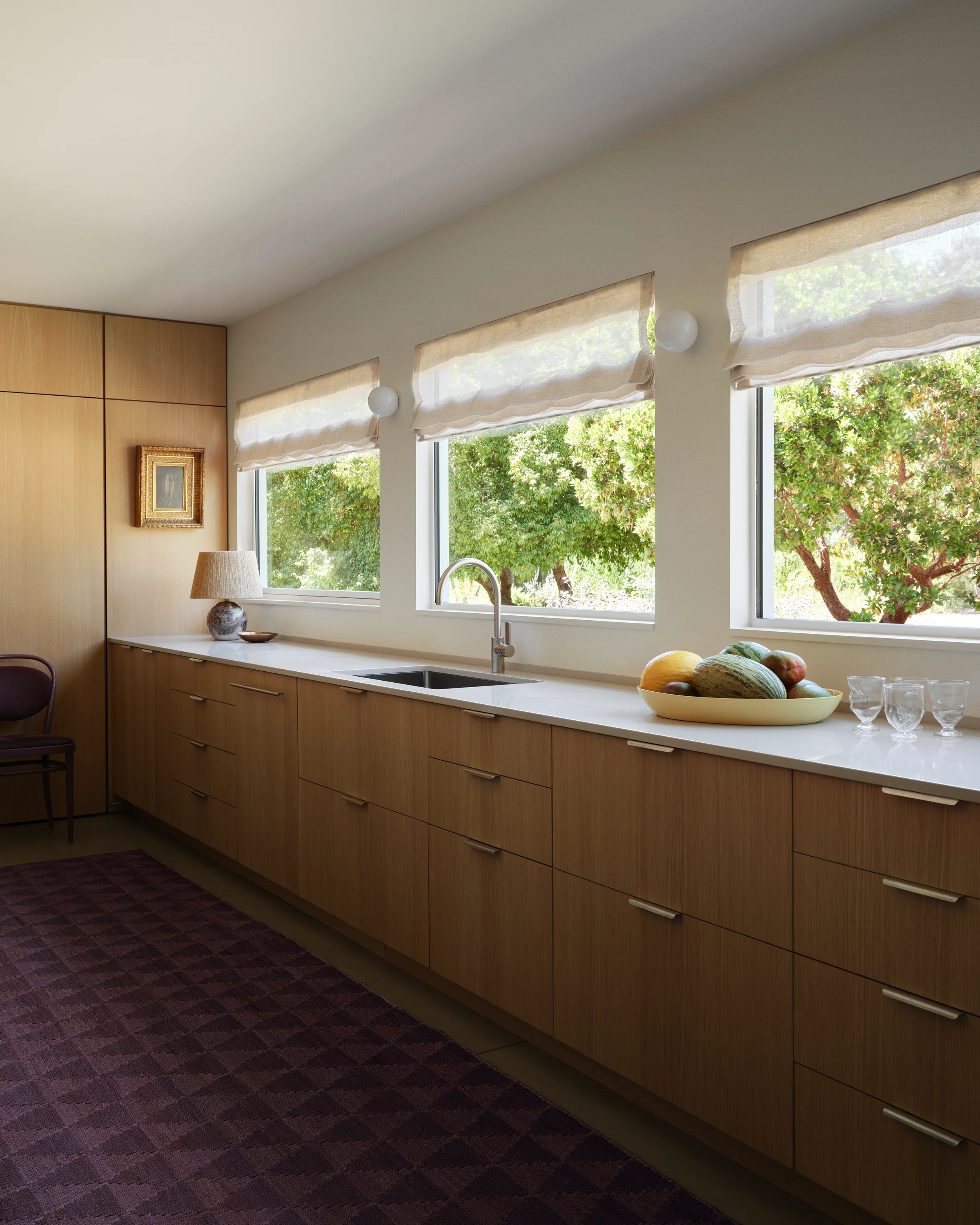 Garden windows illuminate white oak cabinetry and white countertops with vintage purple carpet in modern Sonoma kitchen designed by Chroma.