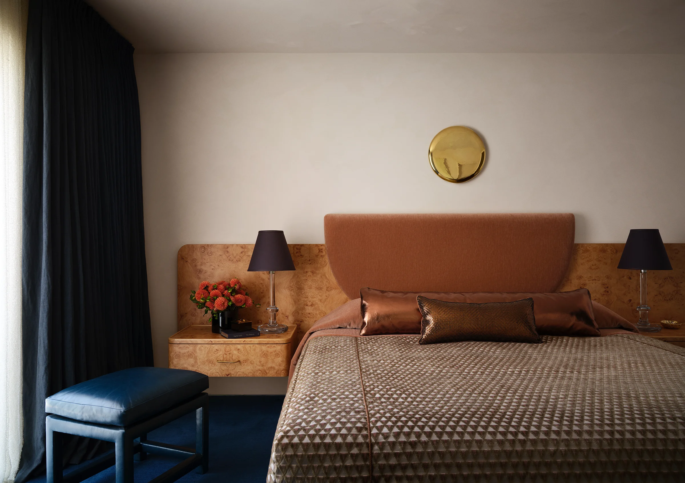 Custom burled wood headboard and floating nightstands paired with vintage lamps, geometric bedding, and polished brass mirror create sophisticated warmth in Sonoma retreat designed by Chroma.