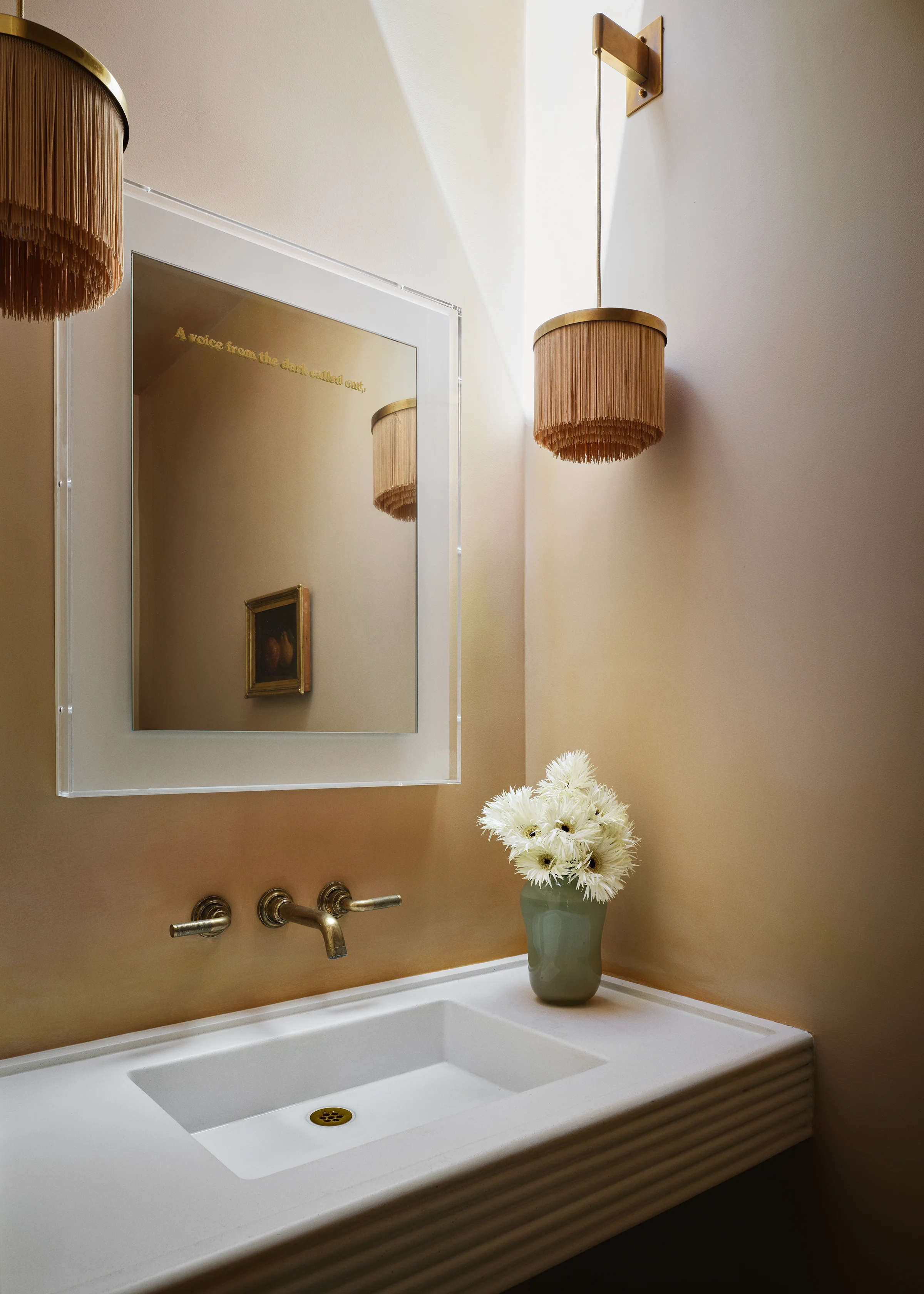 Vintage fringed sconces and artwork with gold leaf text flank a fluted stone vanity with brass fixtures in elegant Sonoma powder room with peachy plaster walls.