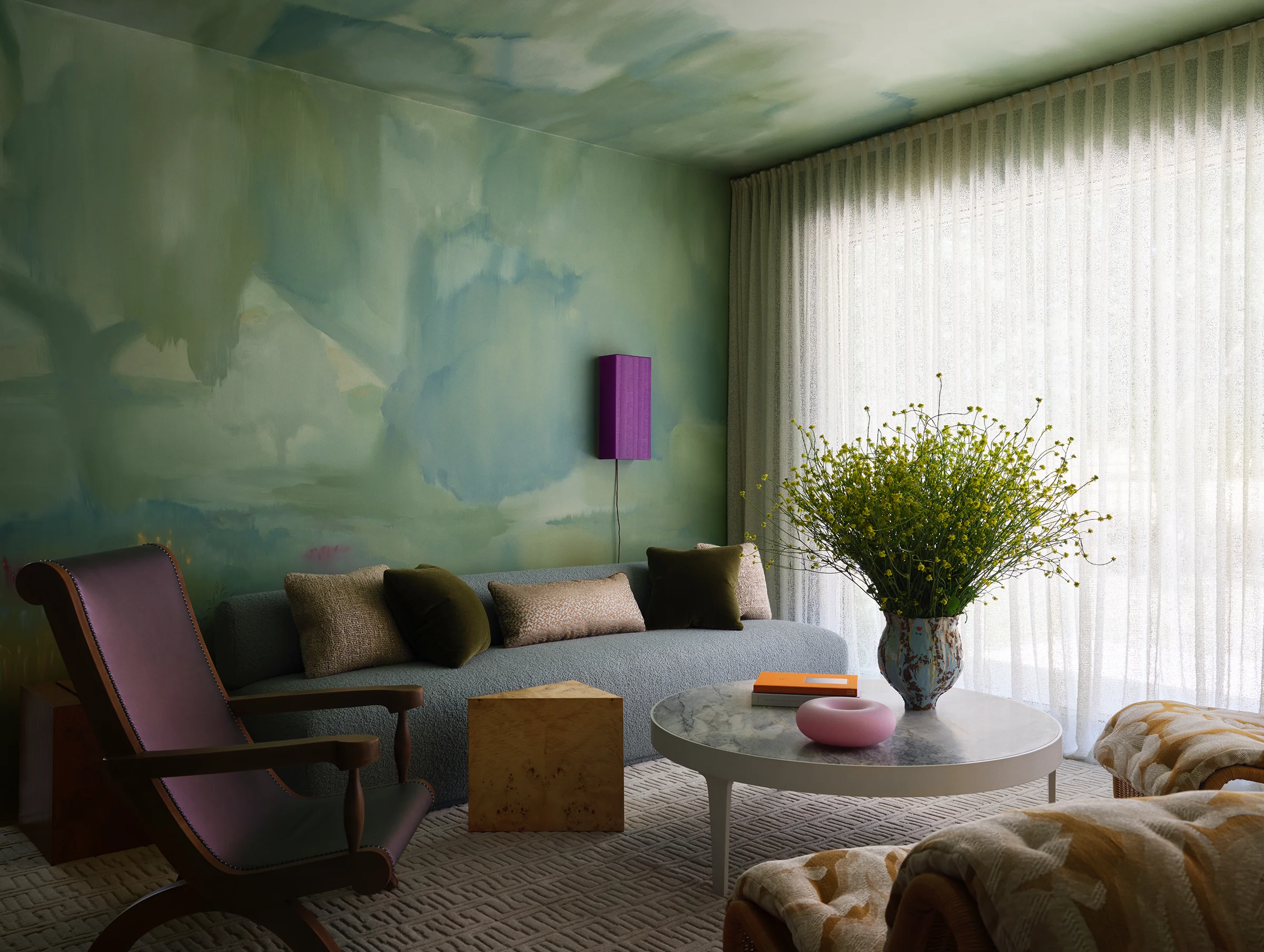 The Endless Summer Custom mural by artist frames a velvet sofa with textural pillows, vintage chair, and cork furnishings beneath flowing curtains in serene Sonoma living room.