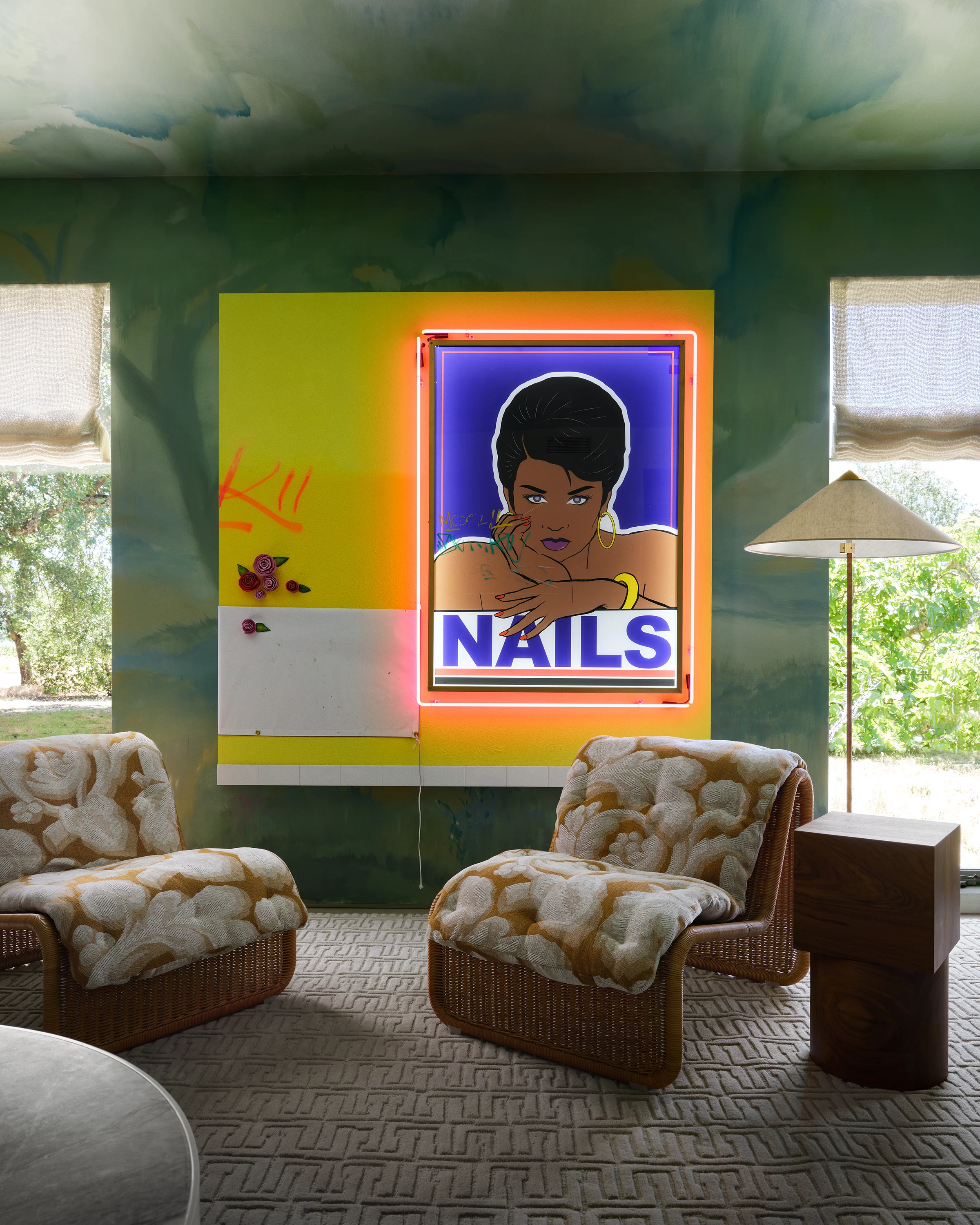 Bold contemporary art with neon lighting punctuates sage green walls framing rattan lounge chairs with textured upholstery in Sonoma ADU designed by Chroma.