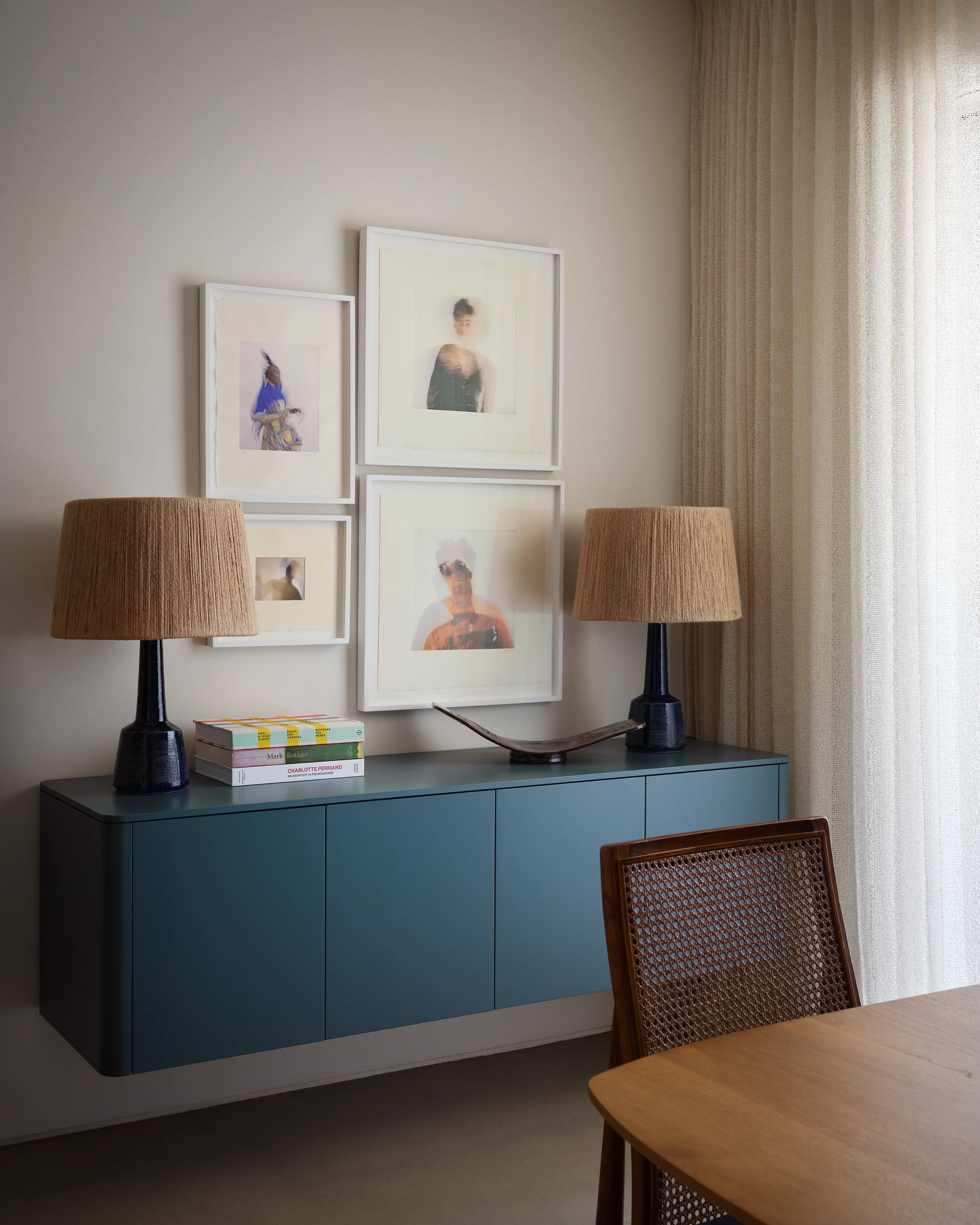 Floating teal credenza styled with portrait photography, rattan lamps, and vintage cane chair creates an elegant vignette in contemporary Sonoma vacation home by Chroma.
