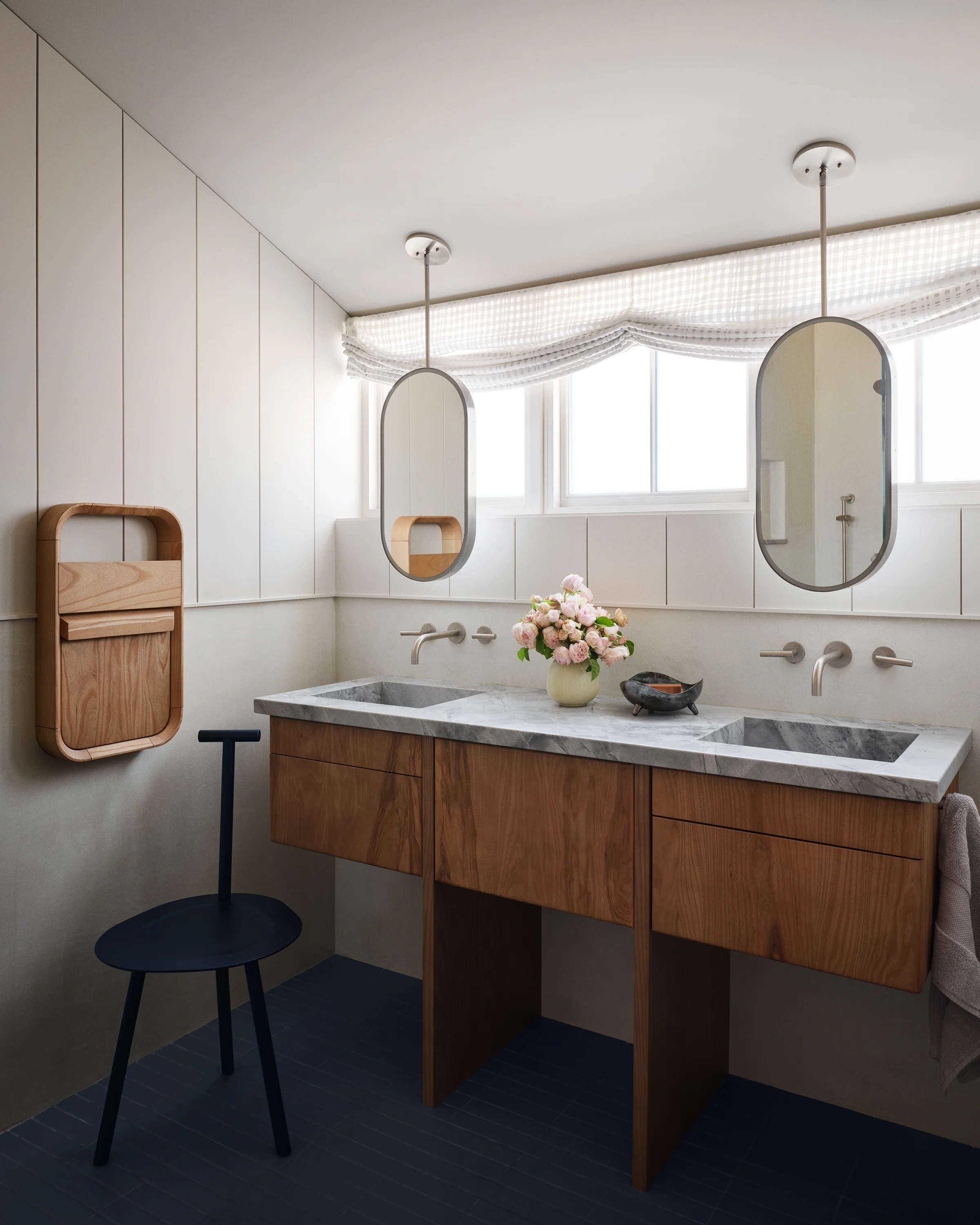 Primary bath with floating walnut double vanity, marble countertop, pill-shaped hanging mirrors, gingham roman shade, and wall-mounted faucets in Santa Cruz cottage by Chroma.