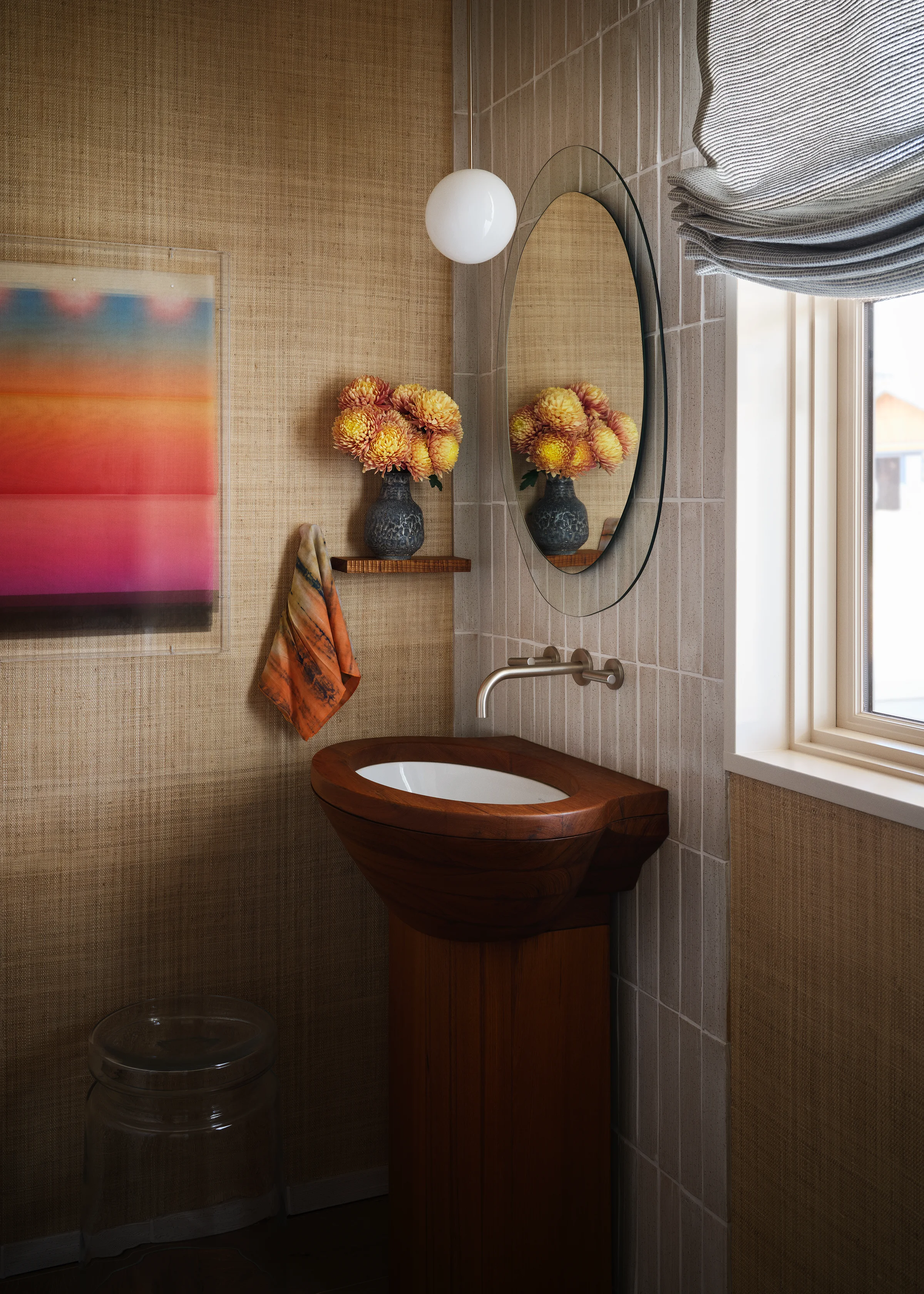 Powder room with custom walnut vessel sink, grasscloth walls, vertical ceramic tile, oval mirror, globe pendant, and vivid gradient artwork in Santa Cruz coastal home by Chroma.
