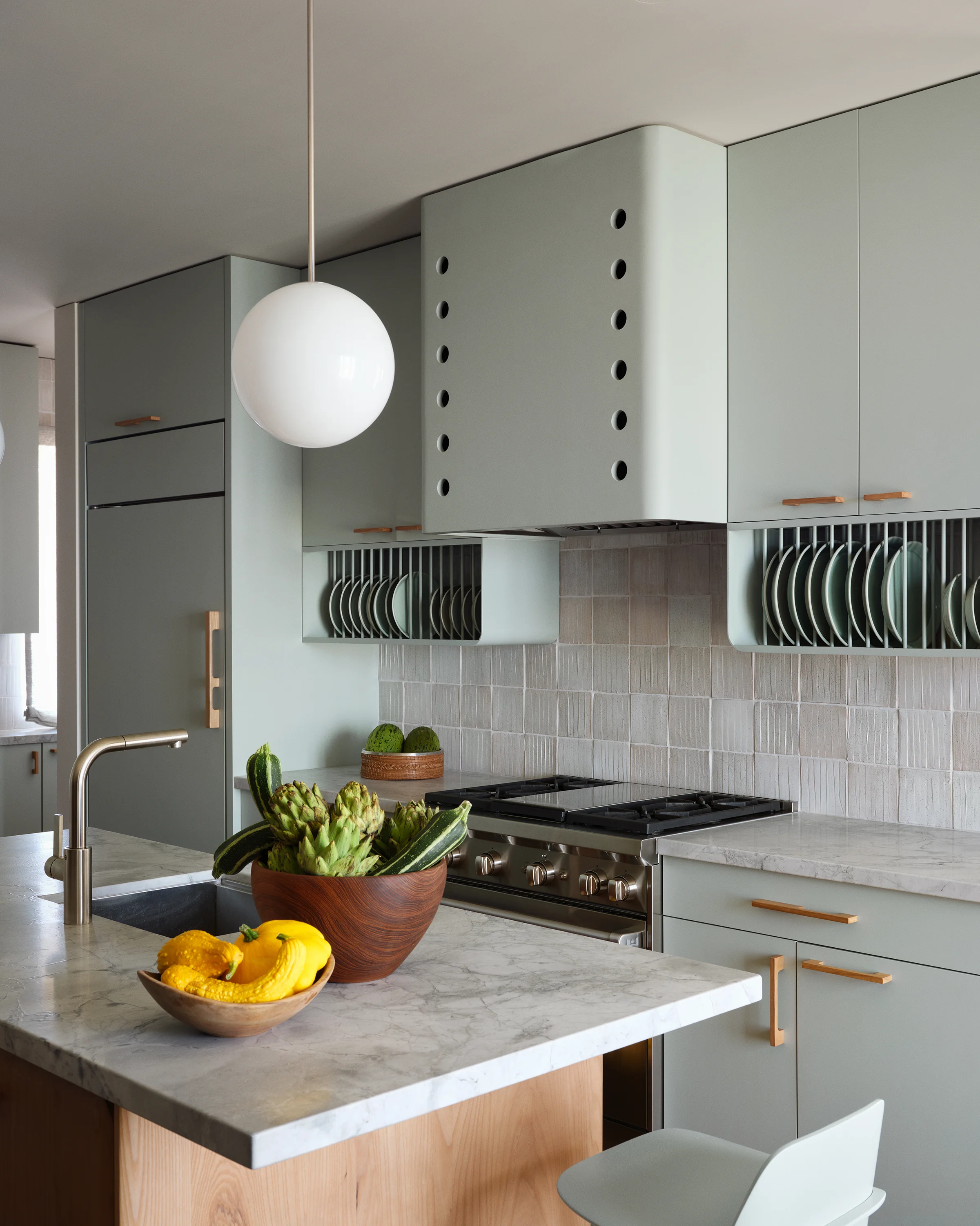 Close detail of sage green kitchen with perforated hood, open ceramic plate rack, marble countertop, ceramic tile backsplash in Santa Cruz home by Chroma.
