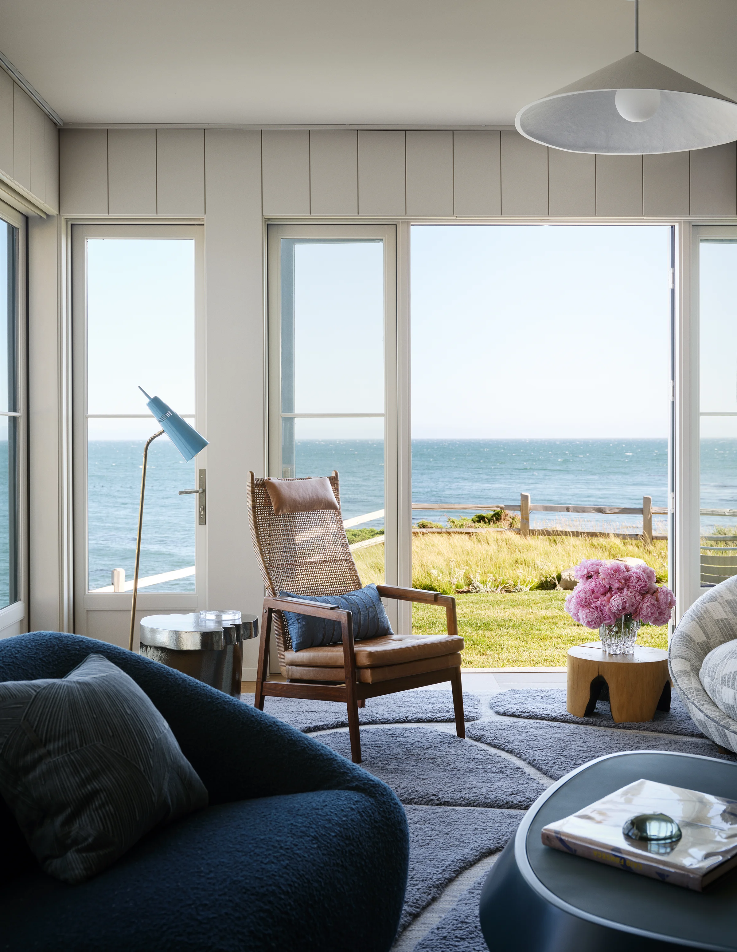 Living room ocean view detail with cane lounge chair, brass vintage floor lamp, and Monterey Bay through floor-to-ceiling windows in Santa Cruz home by Chroma.