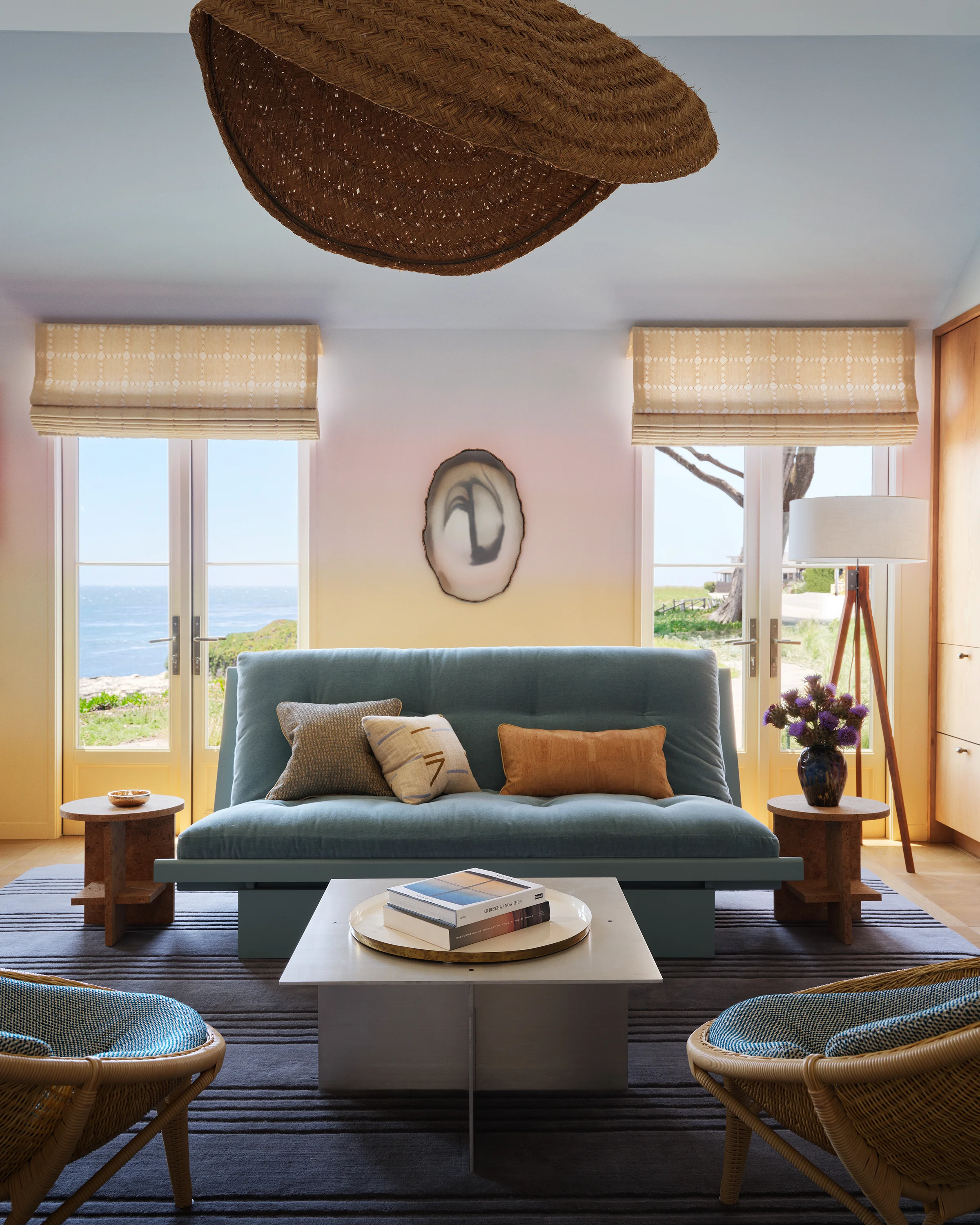 Casita living room with sage mohair sofa, rattan lounge chairs, woven pendant light, agate wall sculpture, and warm golden walls opening to ocean views in Santa Cruz home by Chroma.