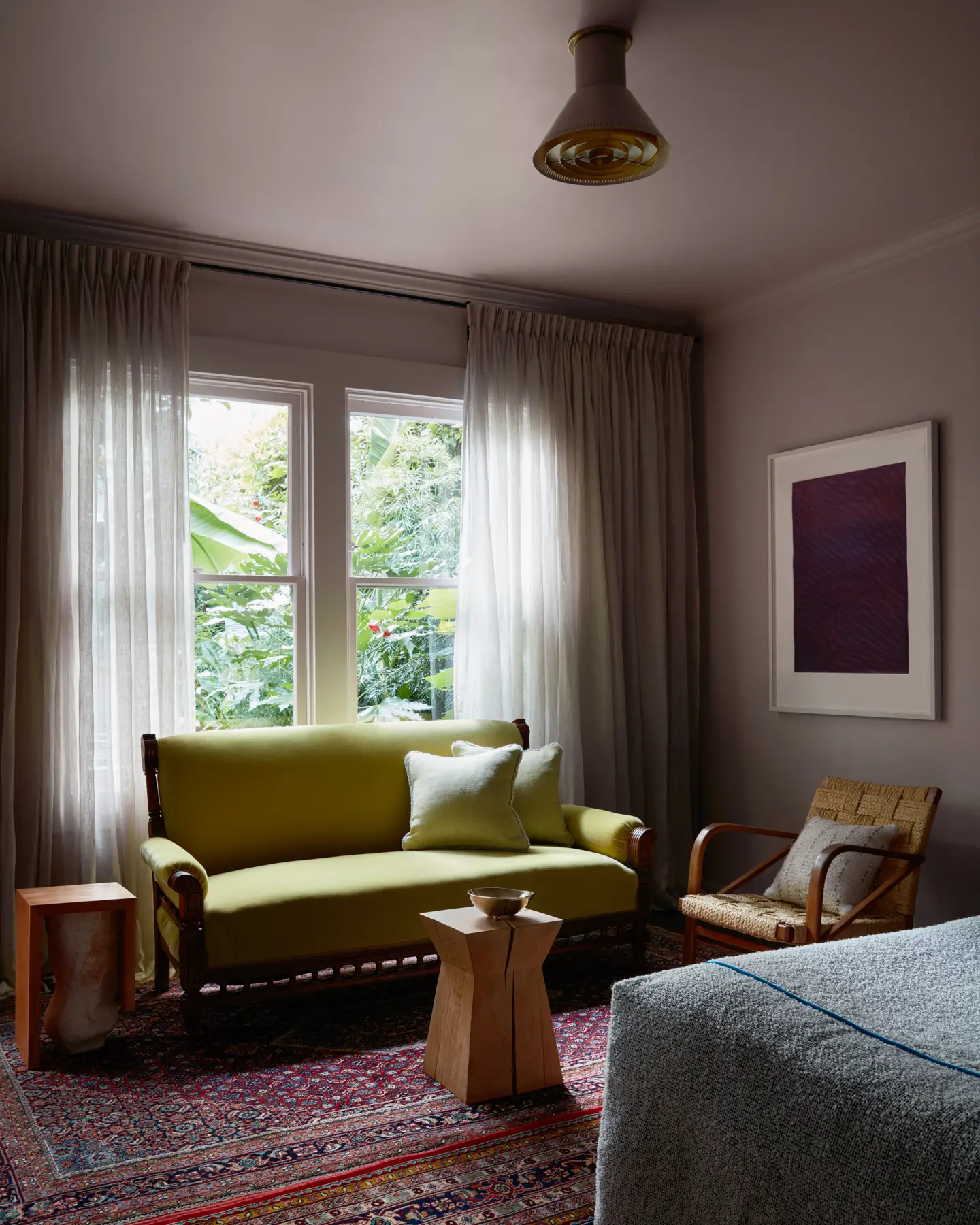 A Paavo Tynell light fixture arrays an Audoux-Minet lounge chair and antique loveseat in chartreuse mohair winged with Christian Liaigre and WHITE DIRT Studio side tables and work by Tauba Auerbach.