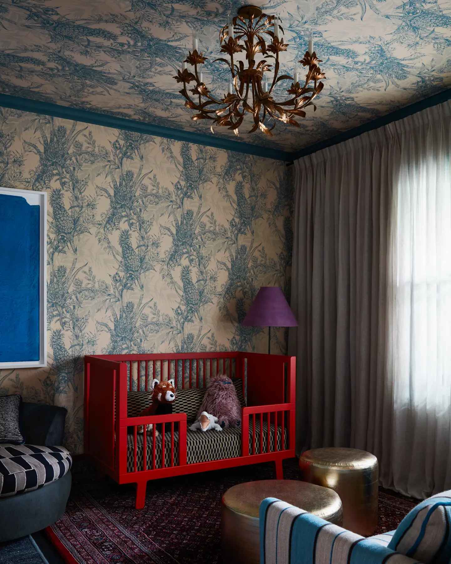 An antique light fixture flounces an unexpected elegance above a bold red Oeuf Sparrow toddler bed conversion with a Pierre Frey Bakou Noir coverlet, gilded by custom ottomans.